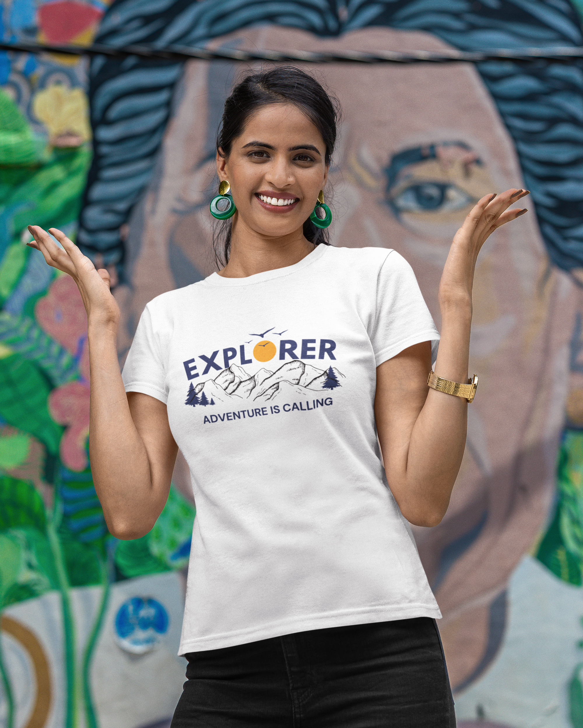 Woman wearing a white t-shirt with 'Explorer Adventure is Calling' design in front of a colorful mural.