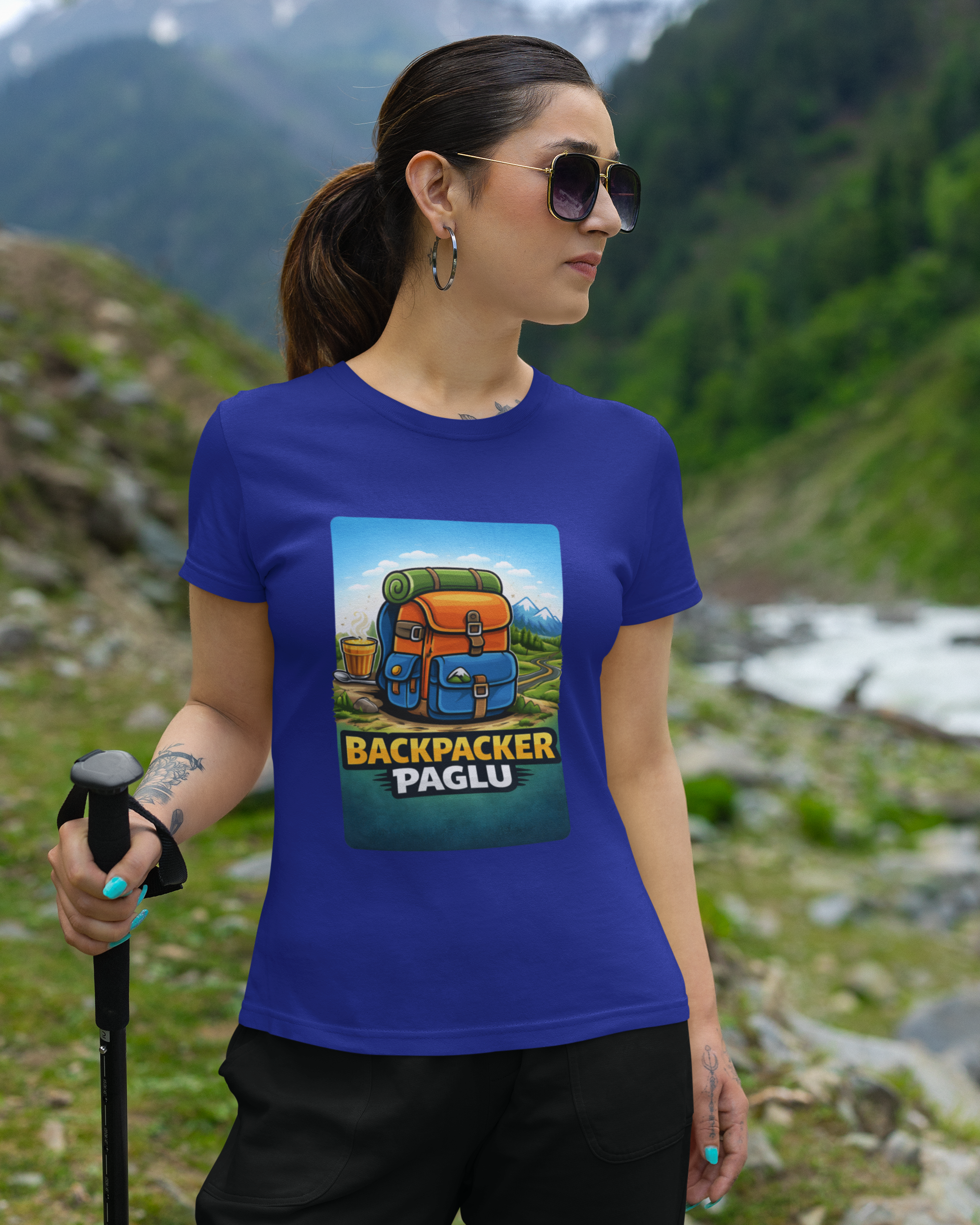 Woman wearing a blue t-shirt with 'Backpacker Paglu' design in a mountainous landscape.