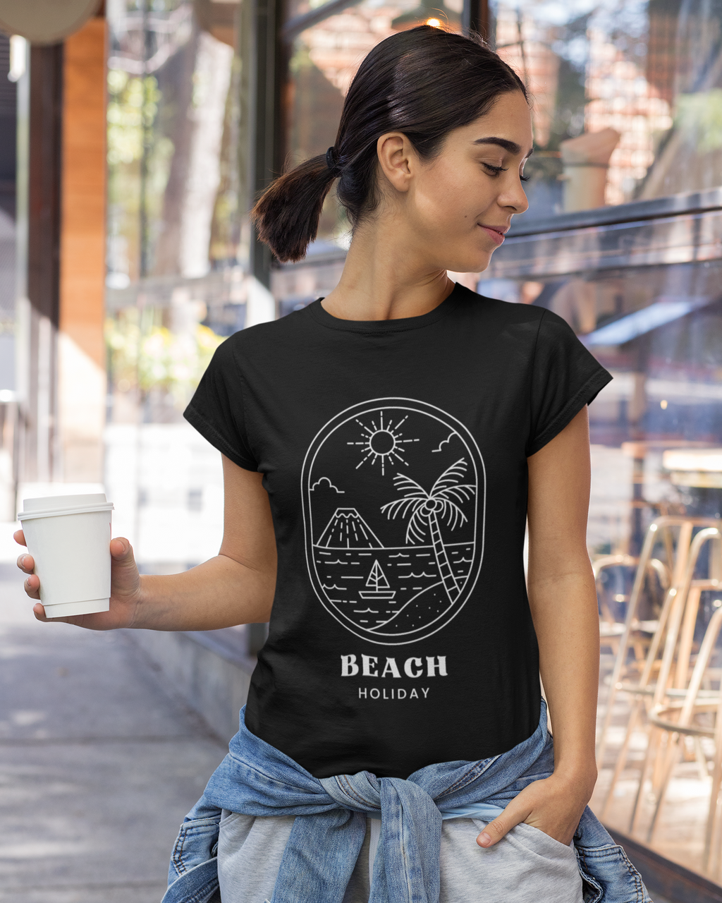 Woman wearing a black t-shirt with 'Beach Holiday' design, holding a cup outdoors.