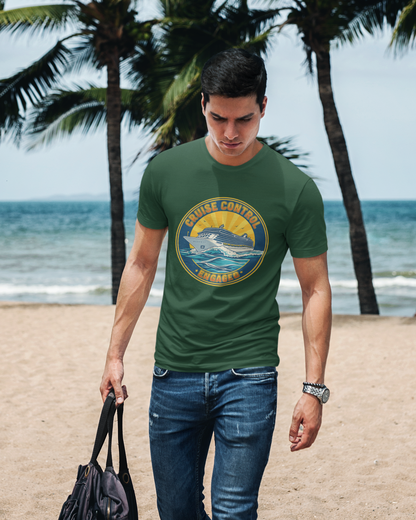 Man walking on a beach wearing a green t-shirt with a logo, holding a black bag.