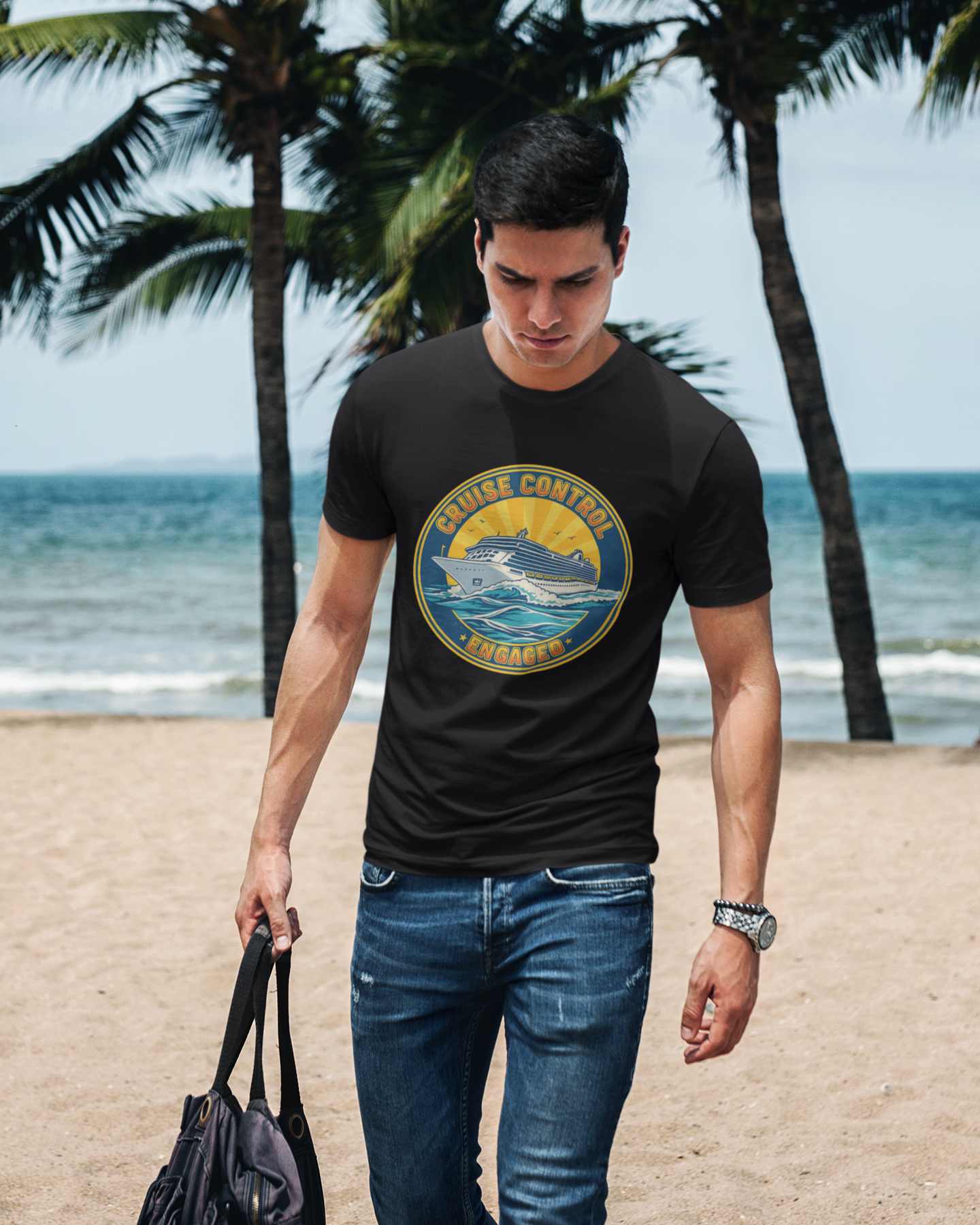 Man walking on a beach wearing a black t-shirt with a graphic design, holding a bag.