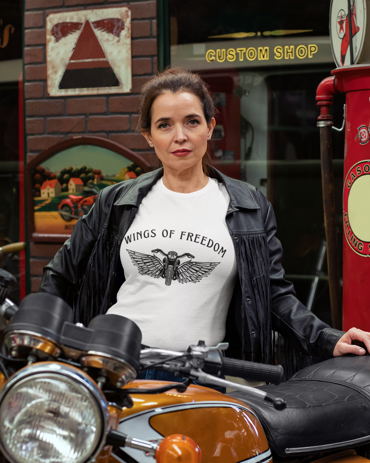 Woman wearing a 'Wings of Freedom' t-shirt sitting on a motorcycle in front of a vintage shop.