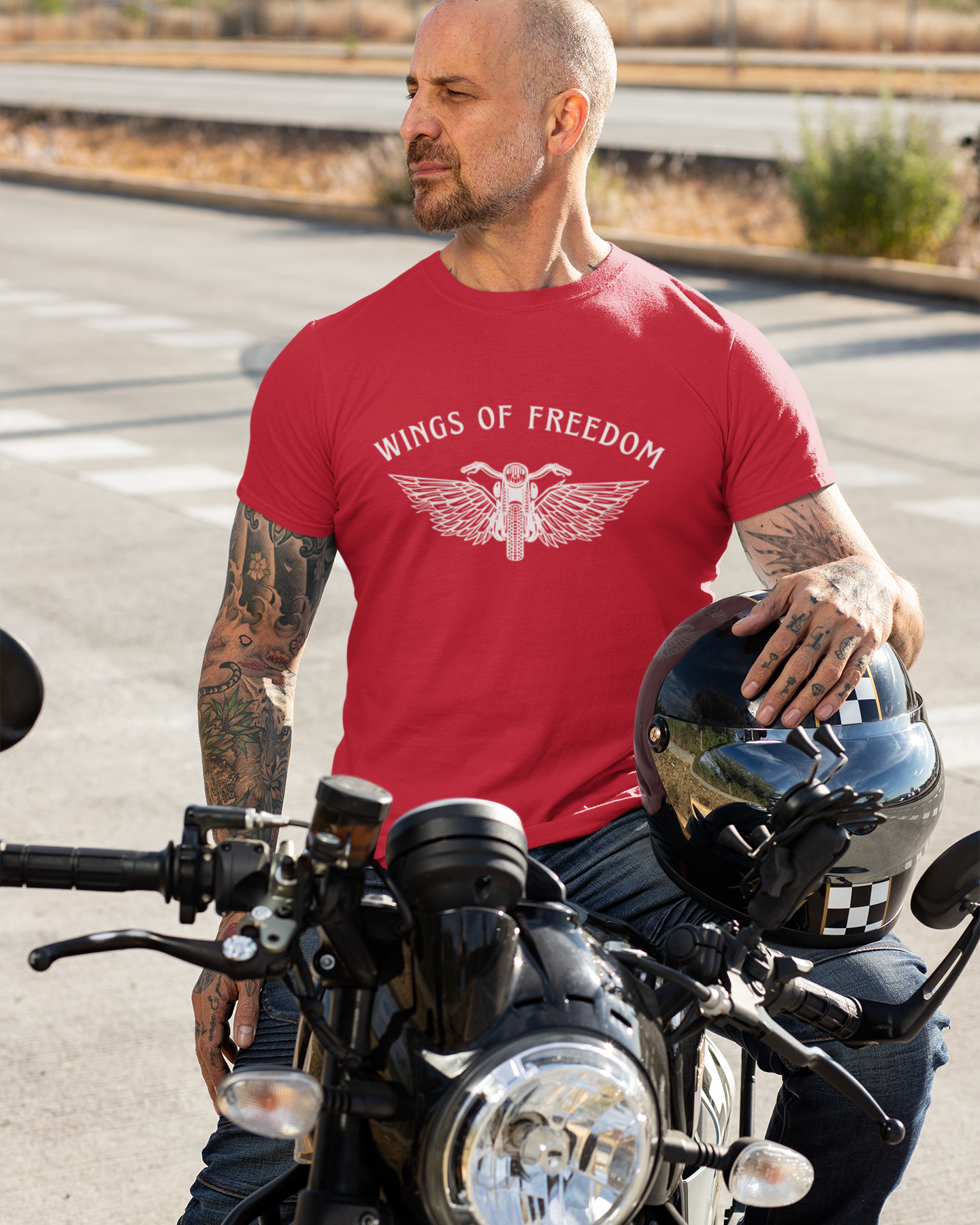 Man wearing a red 'Wings of Freedom' t-shirt sitting on a motorcycle.