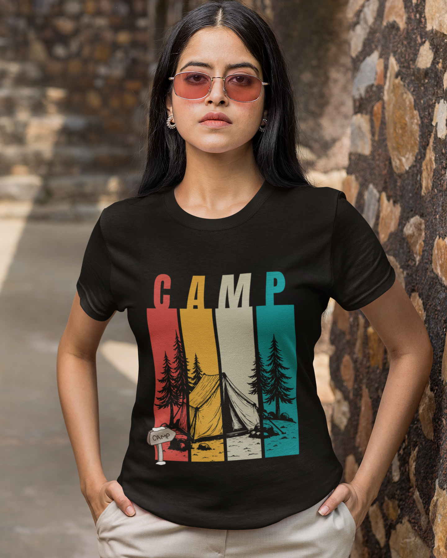 Person wearing a black t-shirt with 'CAMP' and outdoor graphics, standing against a stone wall.